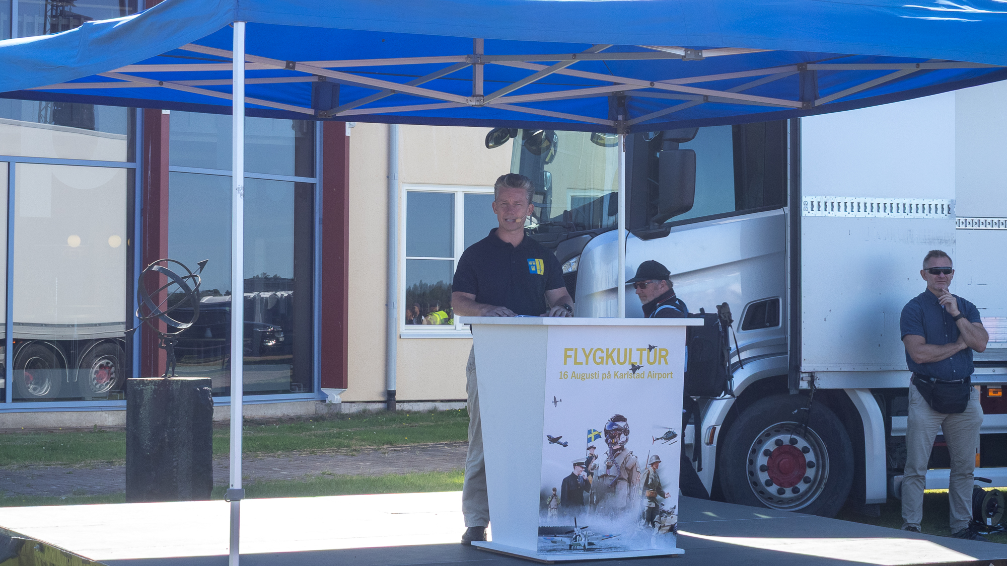 F&ouml;rsvarsminister P&aring;l Jonson st&aring;r i en talarstol med texten Flygkultur p&aring;, p&aring; ett flygf&auml;lt.